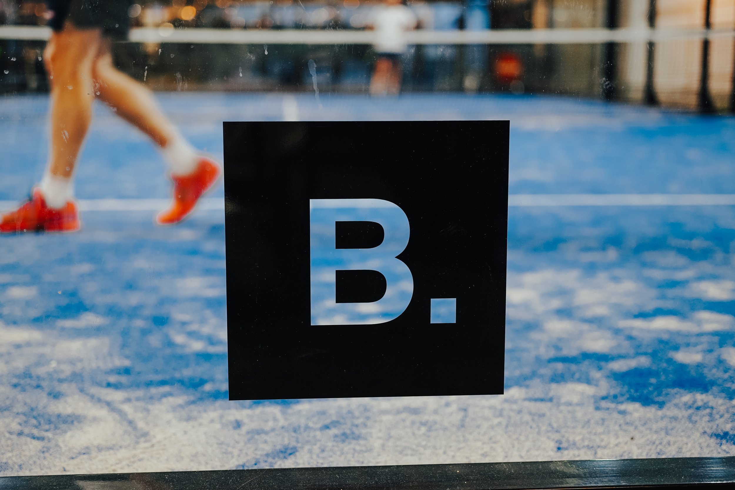 Zwart bord met B.-logo en een rennende speler op de baan