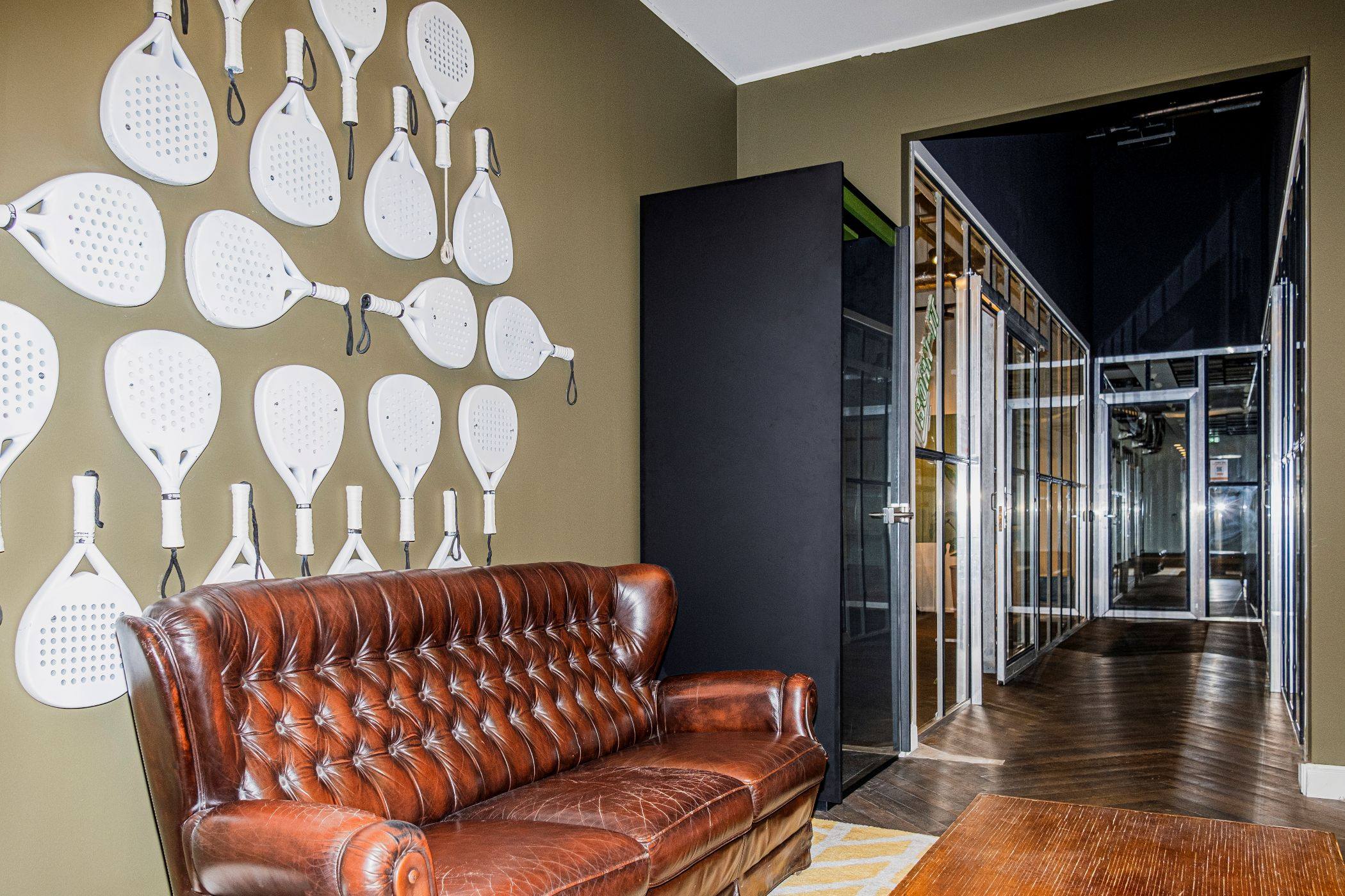 Wand vol witte padelrackets boven een leren bank